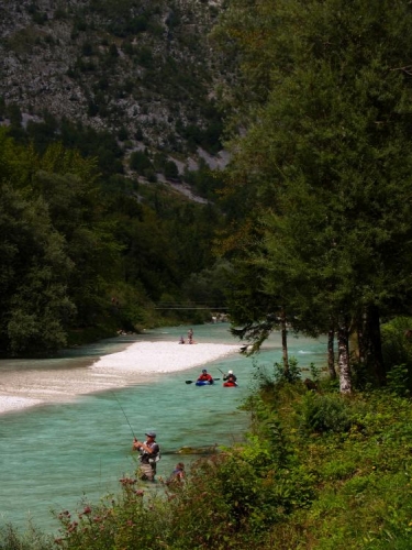 Rybář, kajakáři a v řece se brouzdající turisté u kempu Klin