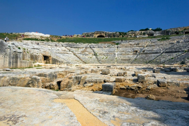 Řecké divadlo. Se stavbou se začalo v 5. stol. př. n. l., ale kompletně bylo divadlo dostavěno v letech 238 – 215 př. n. l. za vlády Hierona tak, že sedadla byla vysekána do skály. Kapacita hlediště byla 16 000 diváků a v průběhu let bylo divadlo mnohokrát upravováno a přestavováno. Za římské vlády bylo divadlo uzpůsobeno i námořním hrám (Naumachie). Původně mělo 61 řad (nyní zbylo 46), rozdělených do 9 sektorů vnitřními schodišti. Šířka hlediště je 138 m a orchestra měla 16 m. Některá sedadla nesou jména předních Syracusanů, např. členů rodiny Hierona II. Nad hledištěm je několik umělých jeskyní, včetně Nymphanea.