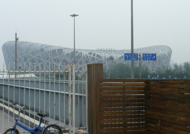 V Pekingu poté, co jsem vylezl z metra na stanici Olympic sports center. V pozadí je olympijský stadion Bird's nest (Ptačí hnízdo), v popředí plot okolo olympijského areálu. Poblíž se nacházela i bezpečnostní kontrola před vstupem do areálu. Tehdy jsem si mylně myslel, že se tam platí za vstup, a tak jsem olympijský areál zbytečně obcházel podél rušných silnic.