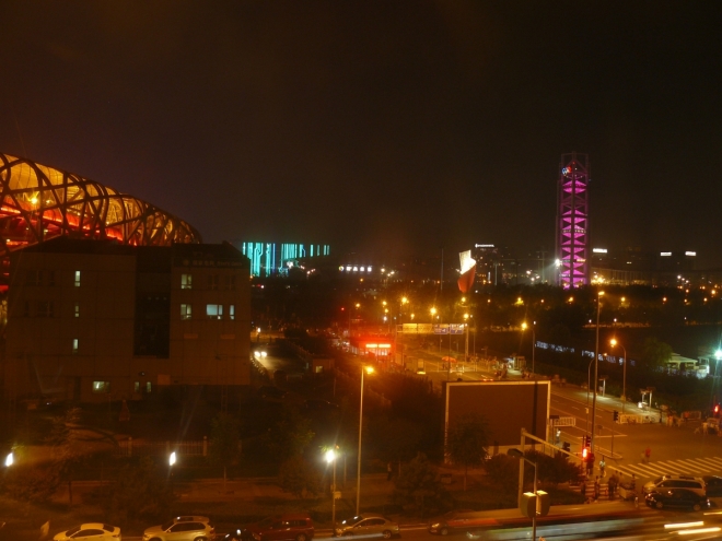 Olympijský areál v noci (vlevo stadion, vpravo rozhledna měnící barvu).