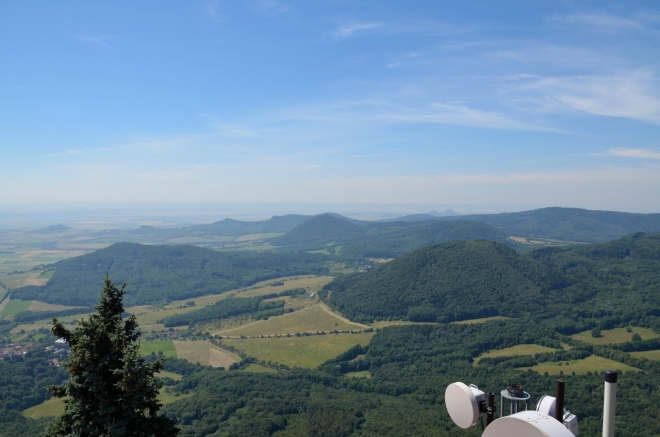 Pohled na jihozápad, v popředí vpravo Milešovský Kloc (674 m) a vlevo Medvědický vrch (též Lhota, 571 m), mezi nimi více vzadu ční Lipská hora (689 m). Informační tabule říká, že v dálce by mohla být nepatrně vidět i Šumava, teď nám ale obzor kvůli oparu končí na 30 až 40 kilometrech.