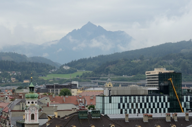 Opodál se z mraků vynořuje rozeklaný vrchol Serles (2717 m), vzdálený asi 16 km.