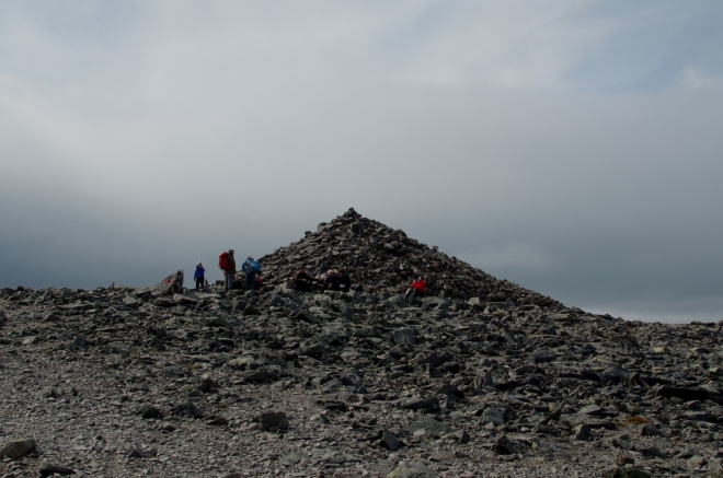 Po asi tři čtvrtě hodině pochodu skoro po rovině se dostáváme na nejvyšší vrchol Besseggenu, Veslfjellet (1743 m). Jeden z důvodů, proč je zde postavena obrovská kamenná mohyla, je nasnadě – jde o významné závětří pro odpočívající turisty.