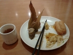 Snídaně na hotelu. Vlevo malý šálek černého čaje, na talíři zleva kukuřice plněná rýží a ještě asi něčím, čínské hůlky, jakási směs zeleniny a nejlepší napodobenina pečiva, jen trochu mastnější.