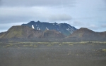 Vnitrozemí Islandu z autobusu cestou do Hrauneyjaru. Kamenitá poušť, občas nějaká zeleň a v dáli vystupující hory.