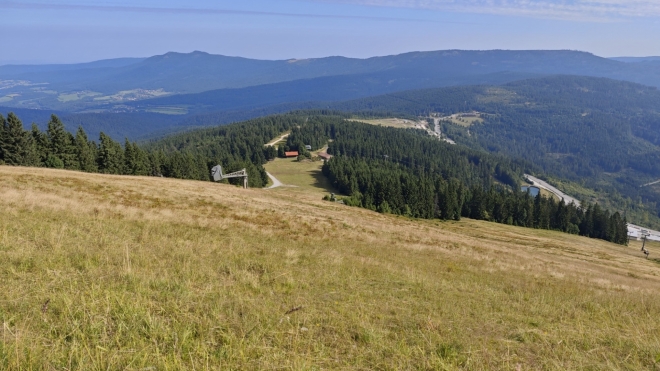Pohled přes sjezdovky k hraničnímu hřebenu. Vlevo dvojvrchol Ostrého.